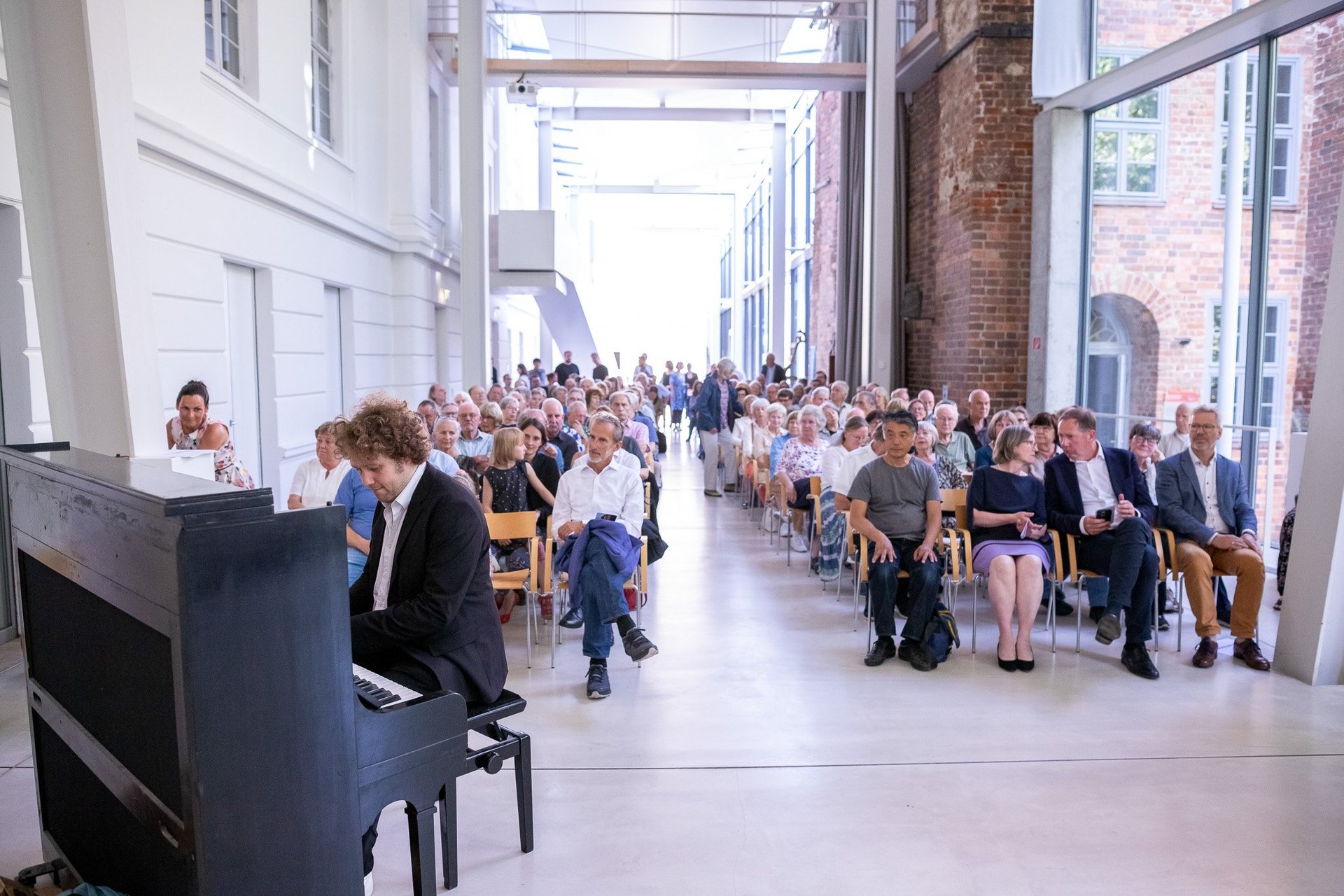 In der linken unteren Bildecke ist ein mann am Klavier zu sehen. Im Hintergrund erstreckt sich die Museumsstraße mit vielen sitzenden Gästen.